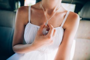 girl wearing white dress while holding pendant of her necklace