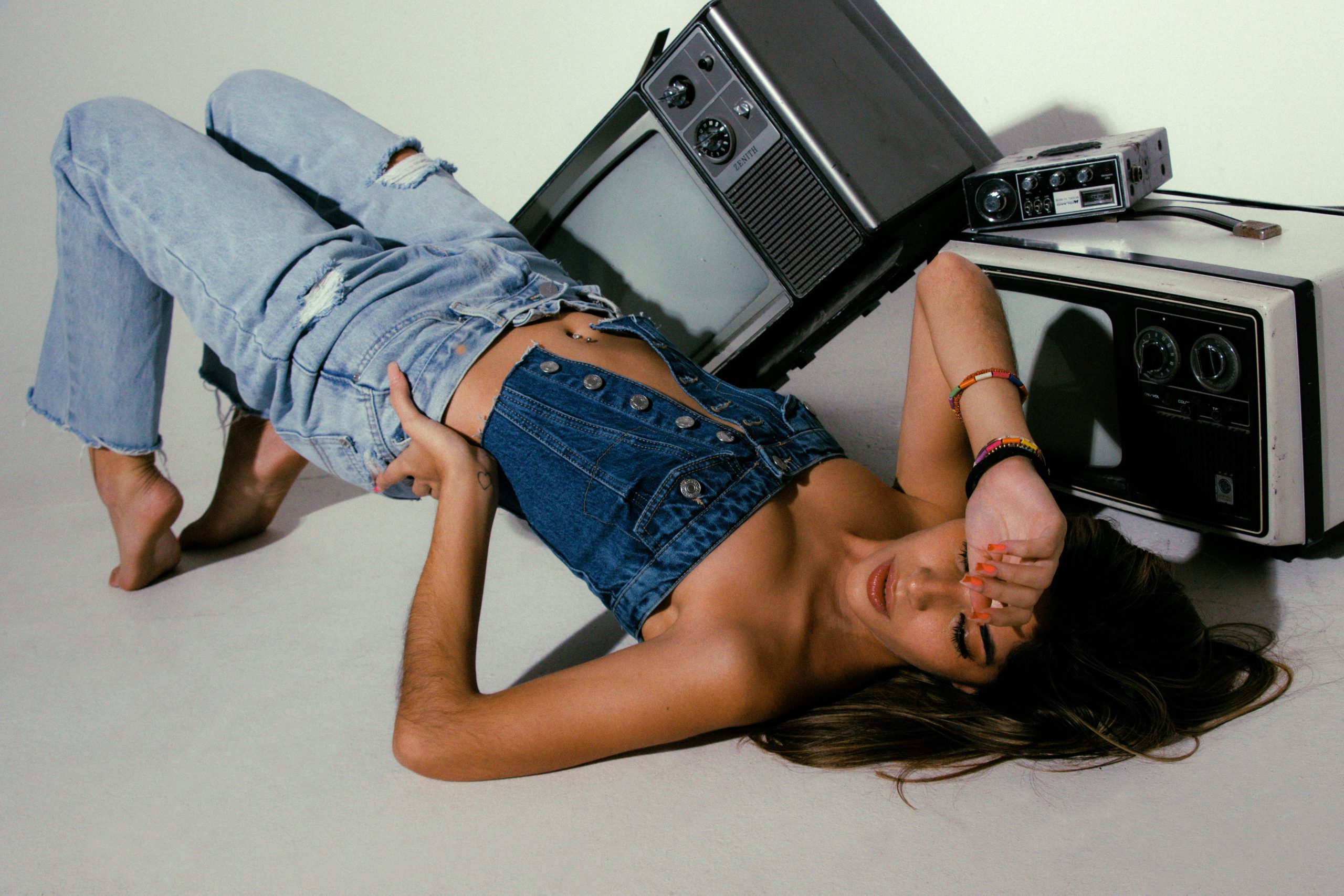 woman wearing a denim tube top and ripped baggy jeans posing for the camera, with vintage entertainment devices in the background