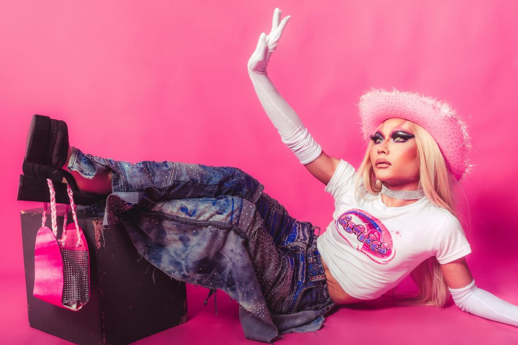 woman wearing a baby tee, baggy jeans, platform sandals, and a pink hat, lying on her side to pose for the camera